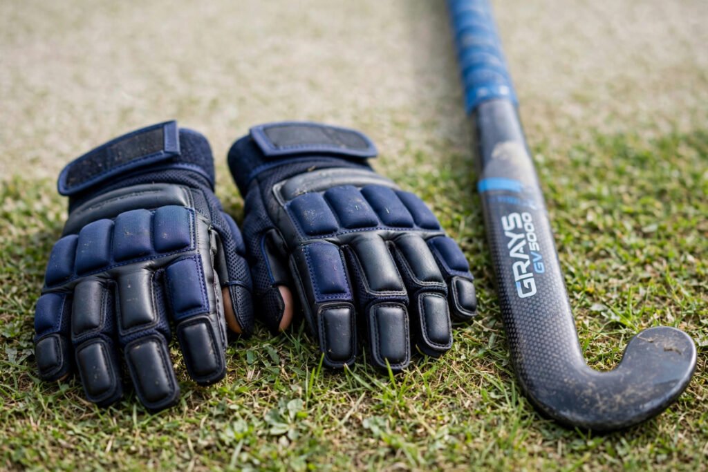 Hockey gloves beside a hockey stick on a pitch