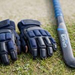 Hockey gloves beside a hockey stick on a pitch